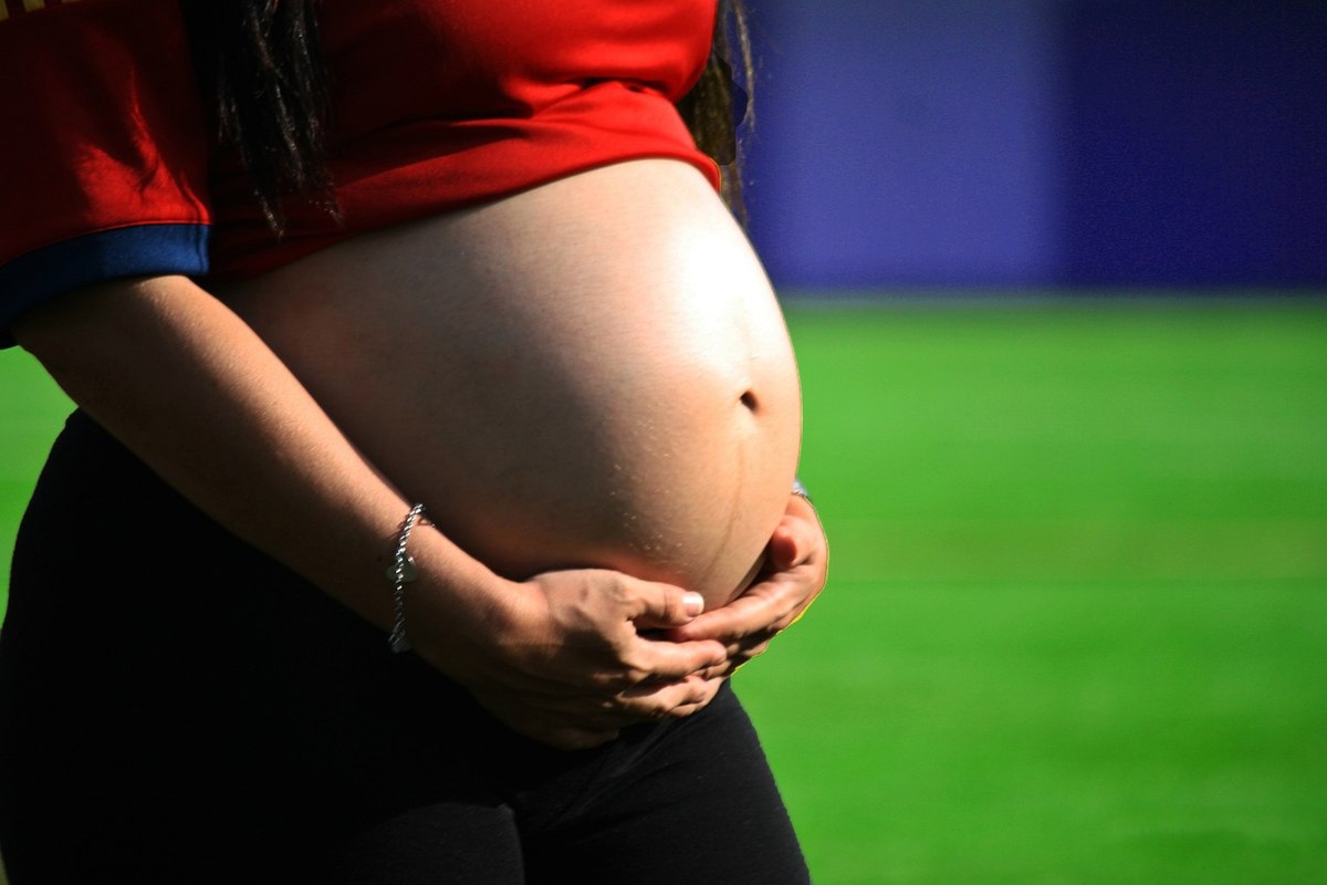 Femme enceinte, mains sur le ventre, vêtue d'une chemise rouge