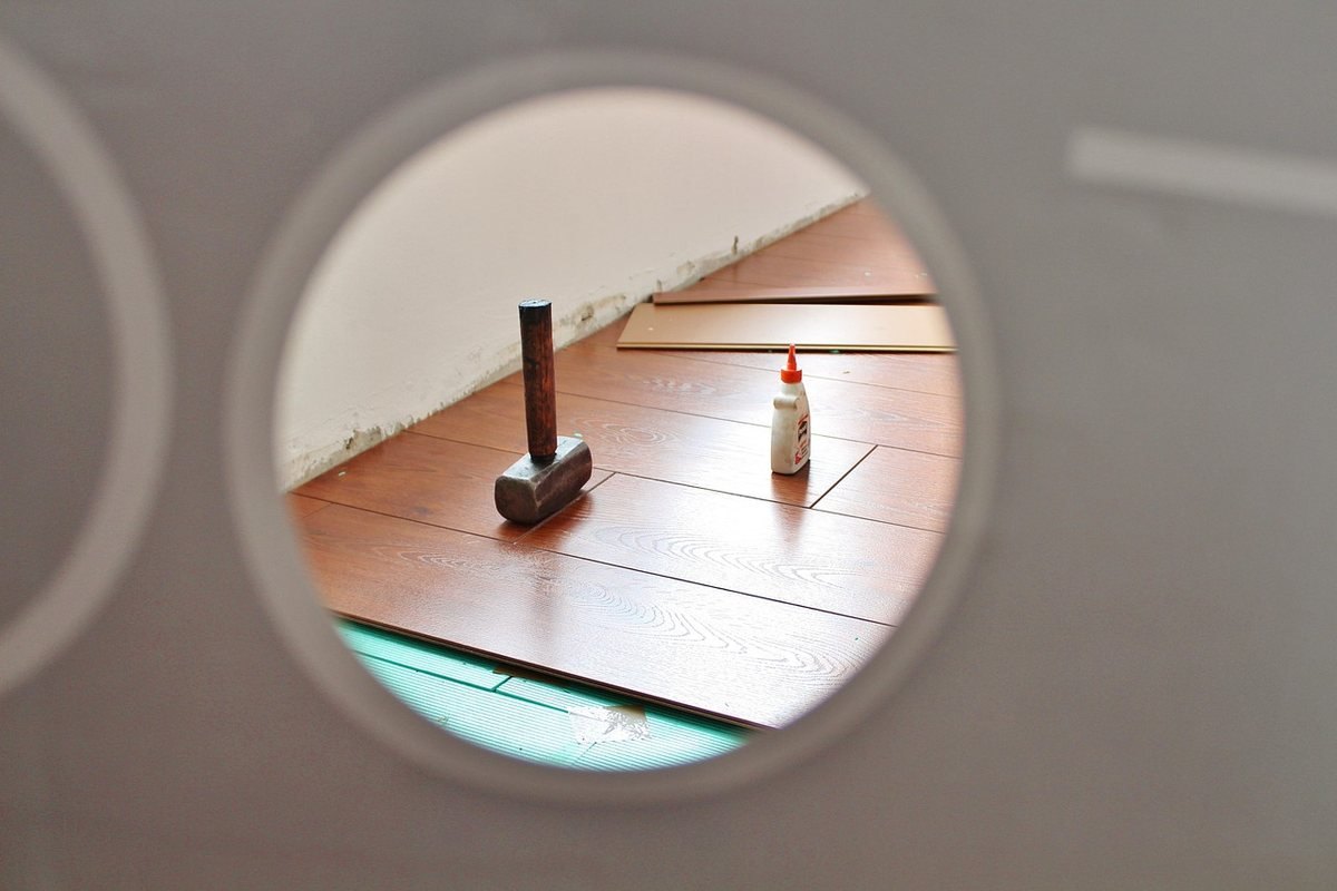 Vue à travers un oeil-de-boeuf sur un atelier avec parquet bois clair et outils de chantier posés au sol Vue à travers un oeil-de-boeuf sur un atelier avec parquet bois clair et outils de chantier posés au sol