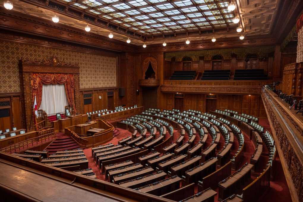 Salle de réunion en bois avec bancs courbes, podium central, rideaux, et éclairage indirect Salle de réunion en bois avec bancs courbes, podium central, rideaux, et éclairage indirect