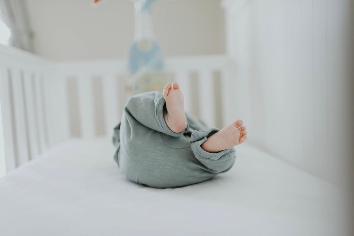 Bébé nu roulant dans un lit blanc, portant un pantalon gris