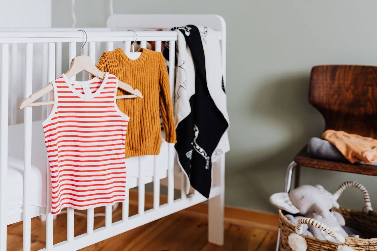 Berceau avec vêtements, jouets dans un panier, chaise en bois près du mur gris