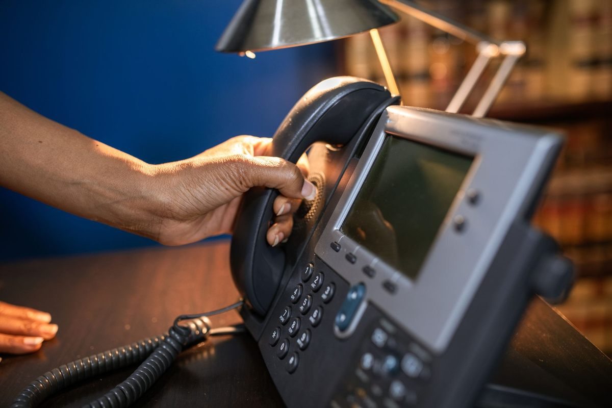 Une main saisit le combiné d'un téléphone de bureau Une main saisit le combiné d'un téléphone de bureau